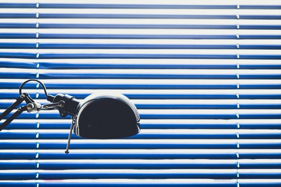 A desk lamp casting light against blue window blinds