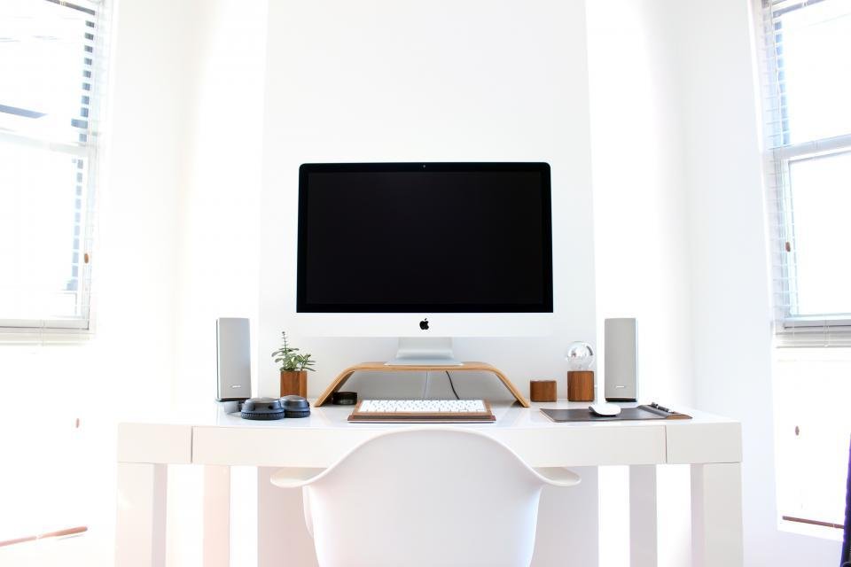 A bright desk with a monitor raised to eye level on a wooden riser