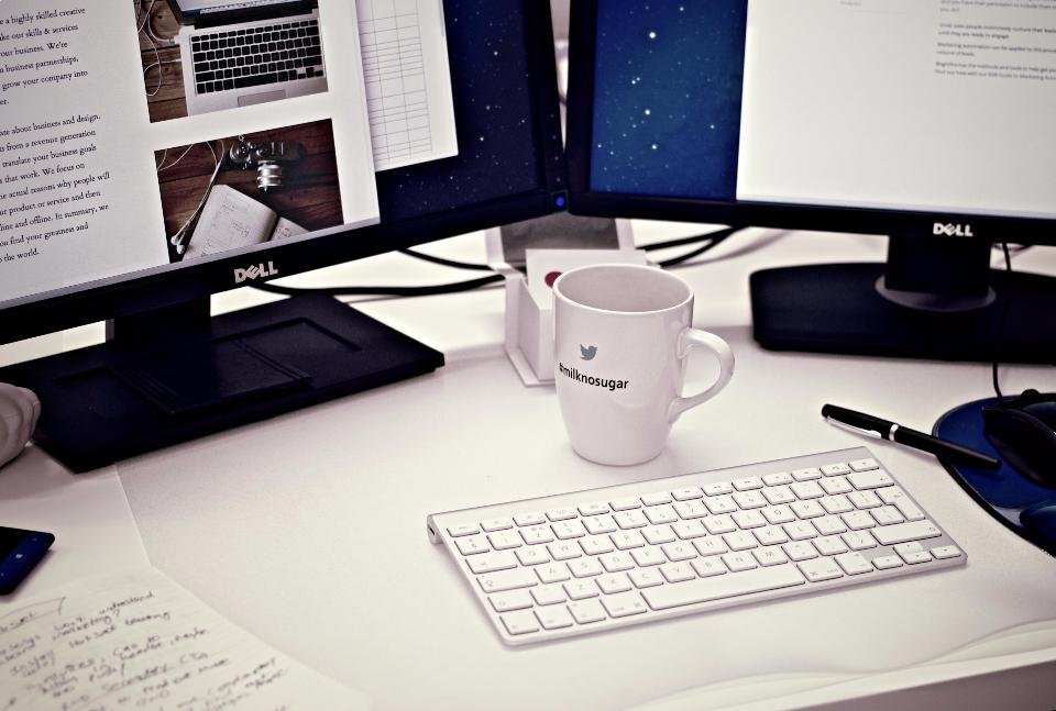 Two monitors on a white desk angled inward toward the chair with a keyboard in front