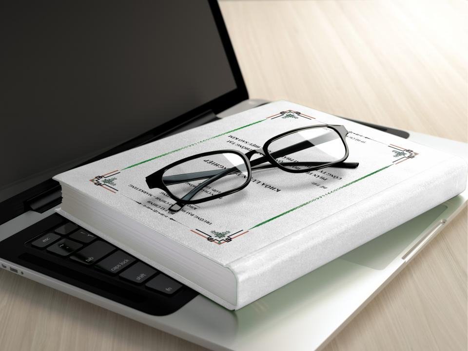 A pair of glasses resting on a closed book on top of a laptop