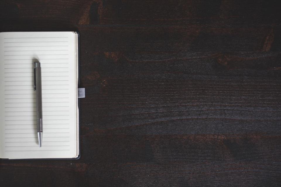 A minimalist desk with a single notebook and pen on dark wood