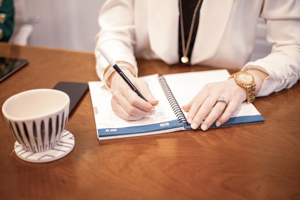 A person planning the day in a paper planner beside a coffee