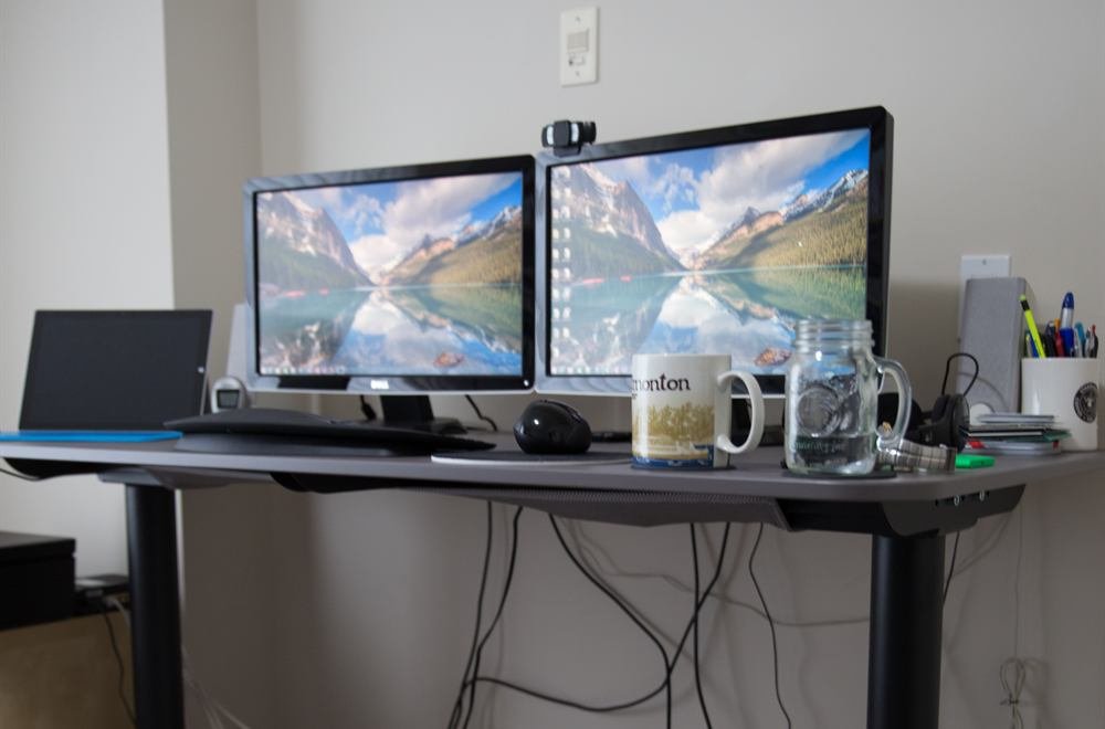 An electric sit-stand desk raised to standing height with dual monitors